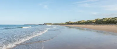 A wide sandy beach curving towards dune grass and a distant headland
